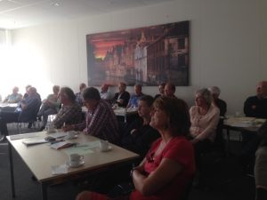 mensen achter tafeltjes in een zaal