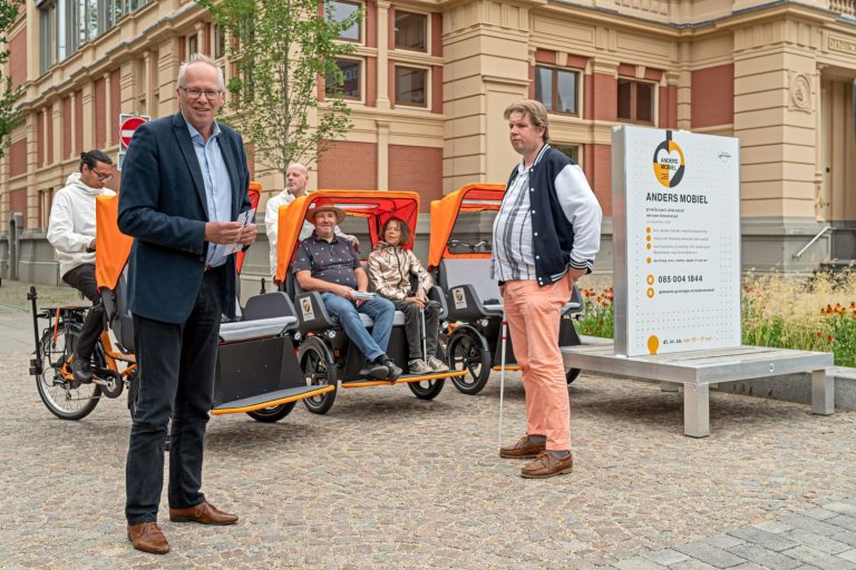 Twee mensen staan voor een fietsriksja met daarin twee personen.